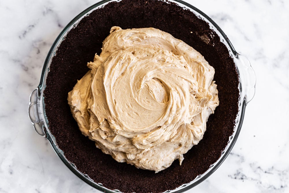 Chocolate graham cracker crust in pie dish with peanut butter filling inside, ready to spread and finish