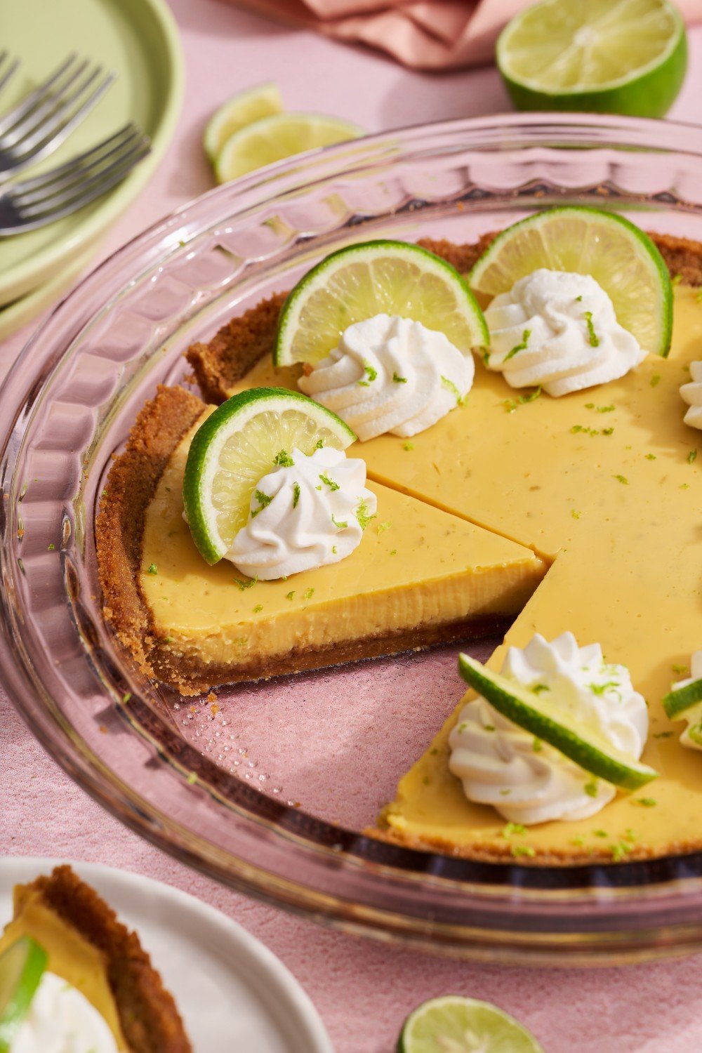 a key lime pie, topped with fresh whipped cream and lime slices, with a slice taken out.