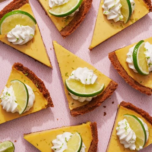 slices of key lime pie, topped with whipped cream and slices of lime, scattered across a light pink background.