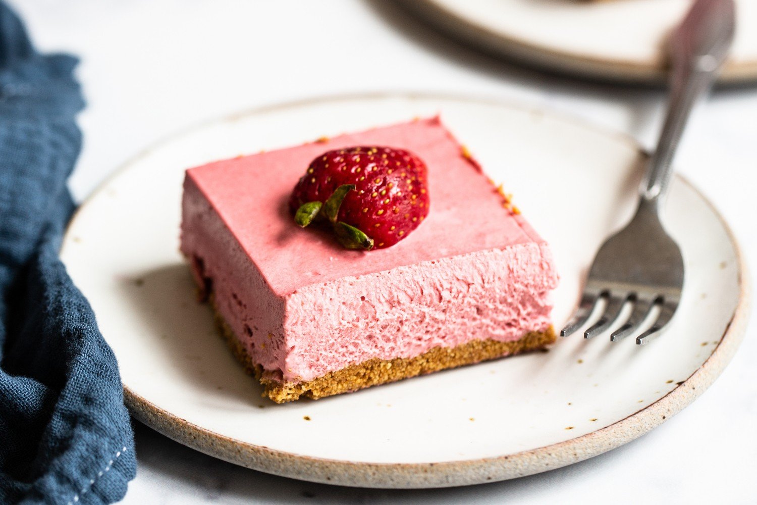 two slices of strawberry cheesecake on white places with forks, ready to serve.