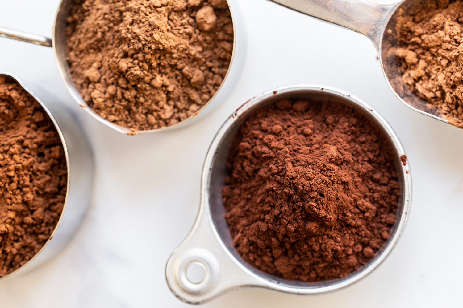 four measuring cups full of cocoa powder on a white background.